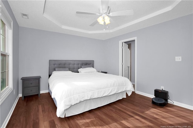 bedroom featuring a raised ceiling, ceiling fan, dark hardwood / wood-style flooring, and a textured ceiling