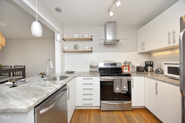 kitchen featuring appliances with stainless steel finishes, sink, wall chimney range hood, pendant lighting, and white cabinets