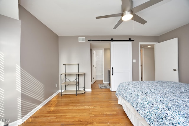 bedroom with a barn door, ceiling fan, and light hardwood / wood-style floors