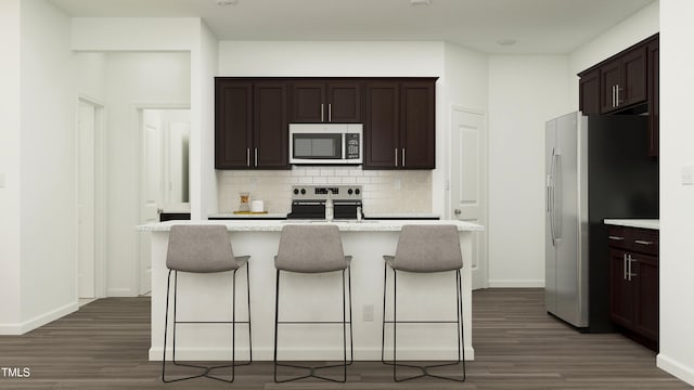 kitchen with stainless steel appliances, dark hardwood / wood-style floors, backsplash, an island with sink, and a kitchen bar