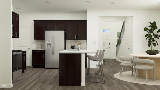 kitchen featuring a kitchen breakfast bar, tasteful backsplash, a center island with sink, stainless steel fridge with ice dispenser, and dark hardwood / wood-style floors