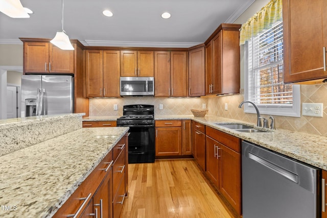 kitchen with light wood-type flooring, ornamental molding, stainless steel appliances, sink, and pendant lighting