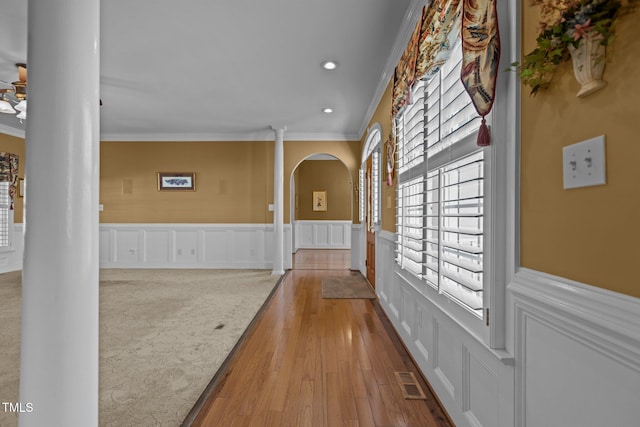 corridor with decorative columns, ornamental molding, and light wood-type flooring