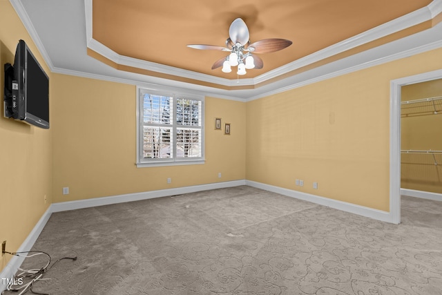 unfurnished bedroom featuring crown molding, a spacious closet, light carpet, a tray ceiling, and ceiling fan