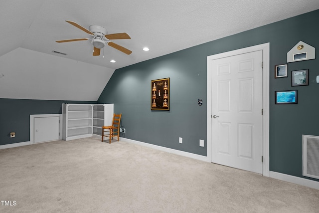 additional living space with vaulted ceiling, light colored carpet, a textured ceiling, and ceiling fan