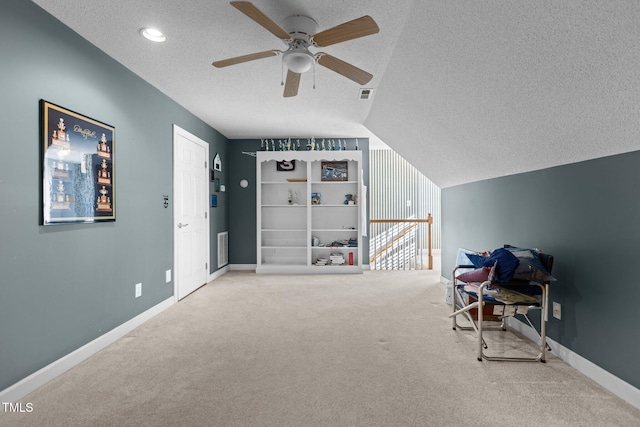 interior space featuring ceiling fan, light colored carpet, lofted ceiling, and a textured ceiling