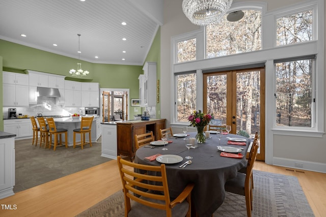 dining space with an inviting chandelier, a towering ceiling, french doors, and a healthy amount of sunlight