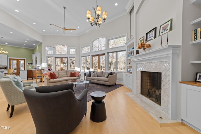 living room with a notable chandelier, ornamental molding, a premium fireplace, and light wood-type flooring