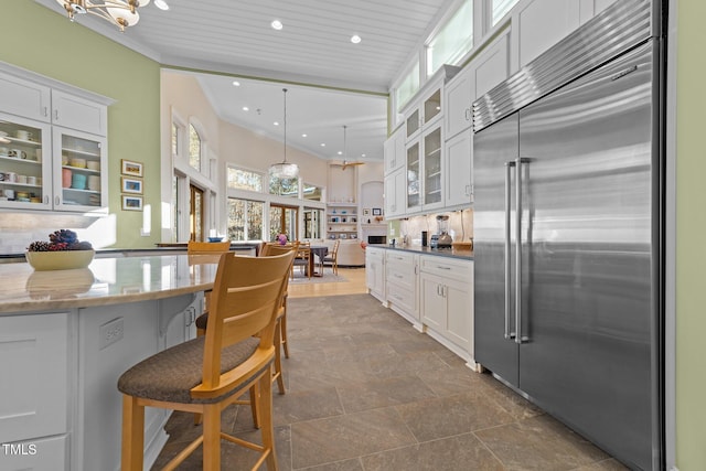 kitchen with a breakfast bar area, white cabinetry, built in fridge, pendant lighting, and light stone countertops