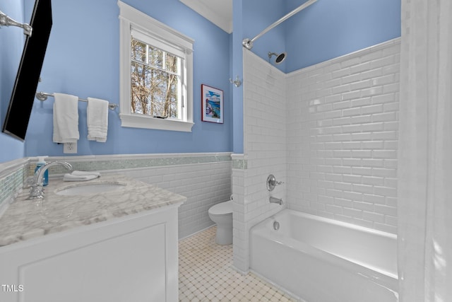 full bathroom featuring tile patterned floors, toilet, tiled shower / bath, tile walls, and vanity