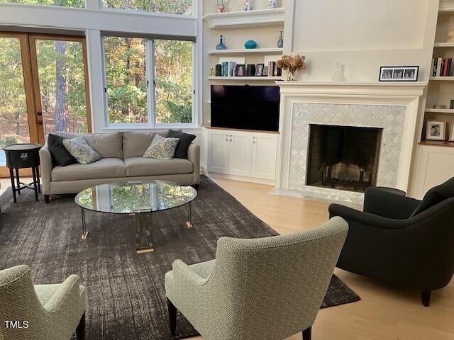 living room featuring a wealth of natural light, built in features, a high end fireplace, and light hardwood / wood-style flooring