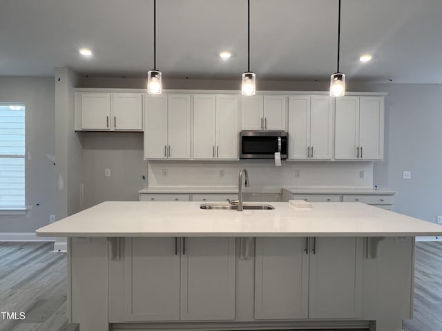 kitchen featuring hanging light fixtures, a center island with sink, light hardwood / wood-style floors, white cabinetry, and sink