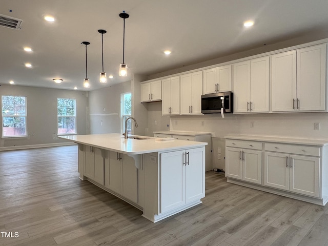 kitchen featuring sink, a center island with sink, white cabinets, and pendant lighting