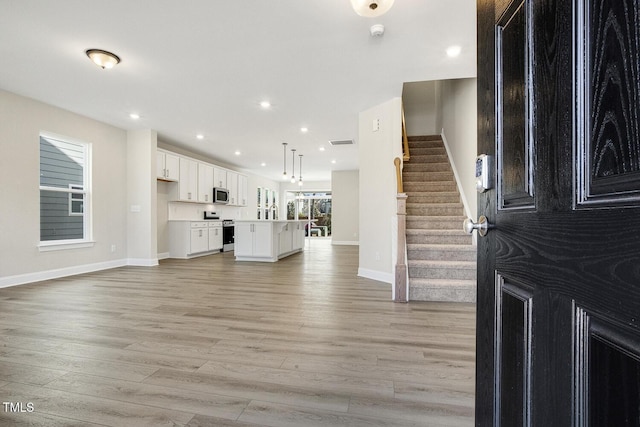 unfurnished living room featuring recessed lighting, visible vents, light wood-style flooring, stairway, and baseboards