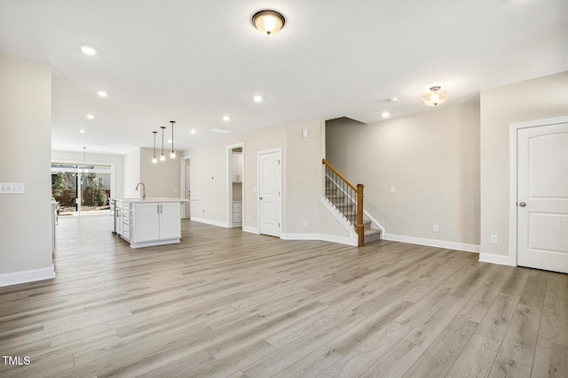 unfurnished living room featuring light wood-style flooring, recessed lighting, a sink, baseboards, and stairway