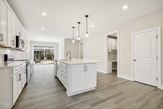 kitchen featuring appliances with stainless steel finishes, a sink, light wood-style flooring, and tasteful backsplash