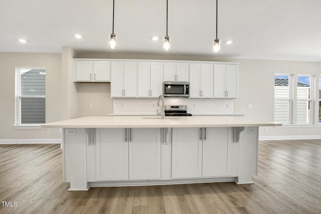 kitchen with a sink, white cabinetry, light countertops, appliances with stainless steel finishes, and a large island with sink