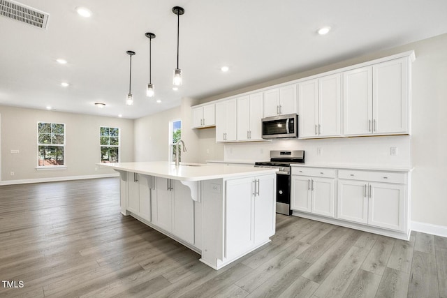 kitchen featuring visible vents, white cabinets, stainless steel appliances, light countertops, and a sink