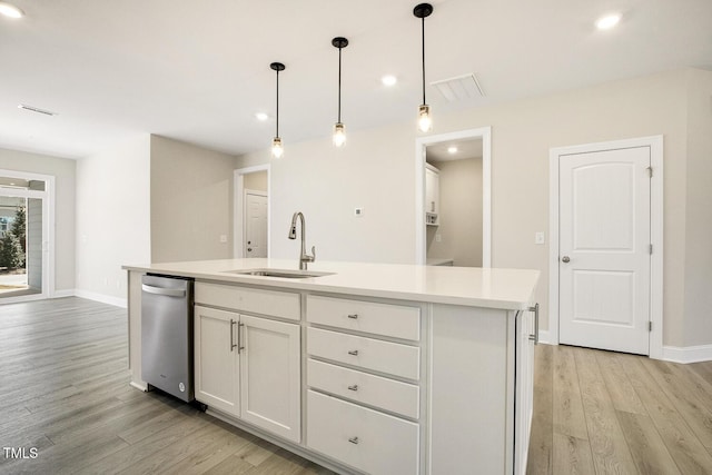 kitchen with a sink, light countertops, stainless steel dishwasher, light wood finished floors, and a center island with sink