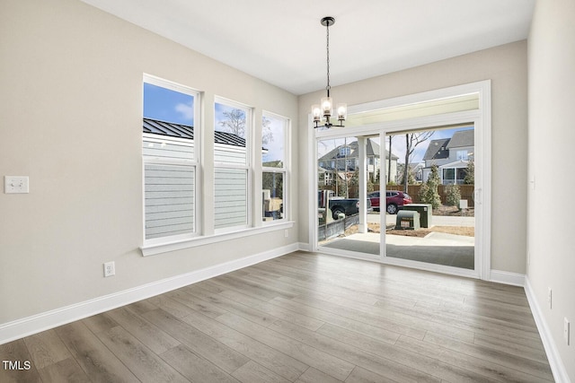 unfurnished dining area featuring an inviting chandelier, baseboards, and wood finished floors