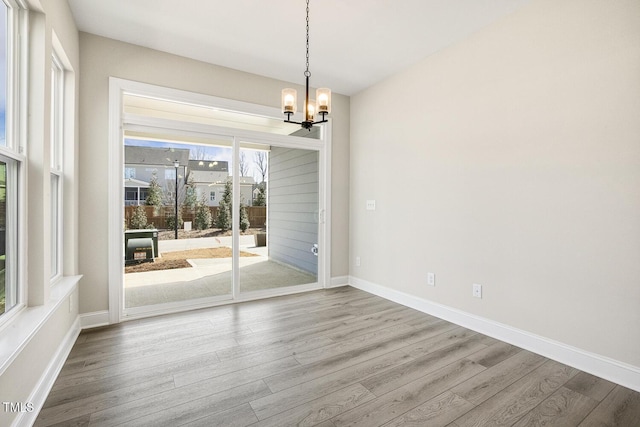 unfurnished dining area with baseboards, wood finished floors, and a notable chandelier