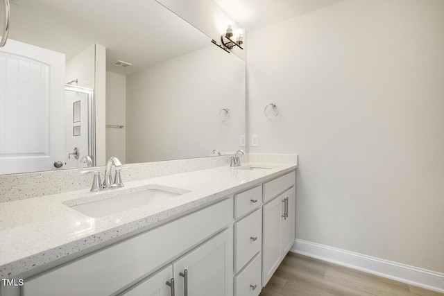 full bathroom featuring double vanity, wood finished floors, a sink, and baseboards