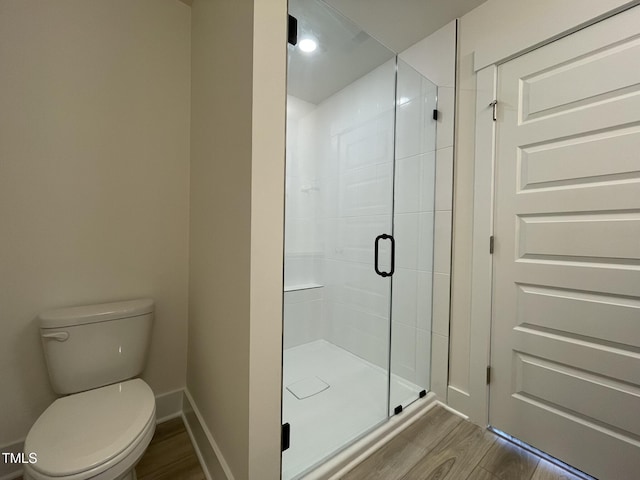 bathroom with toilet, a stall shower, baseboards, and wood finished floors