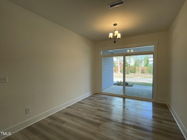 unfurnished room featuring an inviting chandelier, dark wood-type flooring, baseboards, and visible vents