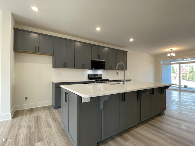 kitchen featuring stainless steel range with gas stovetop, black microwave, light wood-style floors, and a sink