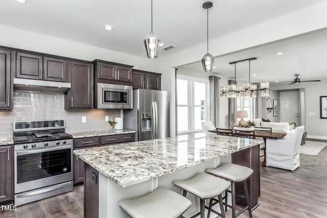 kitchen featuring dark brown cabinetry, ceiling fan, a center island, dark hardwood / wood-style flooring, and appliances with stainless steel finishes