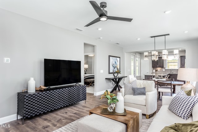 living room with hardwood / wood-style floors, ceiling fan with notable chandelier, and sink