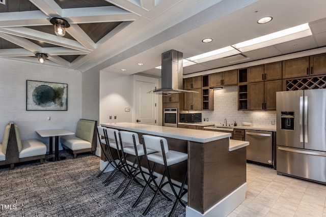 kitchen featuring a breakfast bar, a kitchen island, appliances with stainless steel finishes, island range hood, and dark brown cabinetry