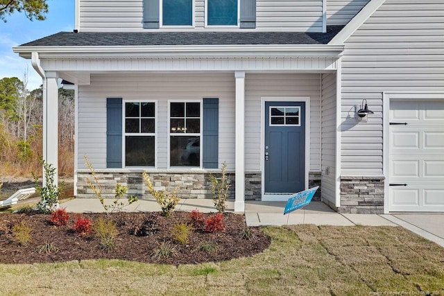 doorway to property with covered porch, stone siding, roof with shingles, and an attached garage