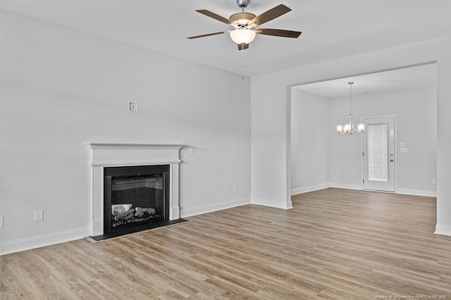 unfurnished living room with a fireplace, baseboards, wood finished floors, and ceiling fan with notable chandelier