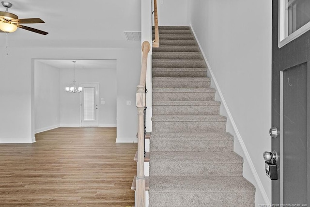 stairs with ceiling fan with notable chandelier, wood finished floors, and baseboards