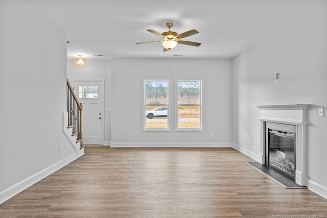 unfurnished living room featuring baseboards, stairway, wood finished floors, and a glass covered fireplace