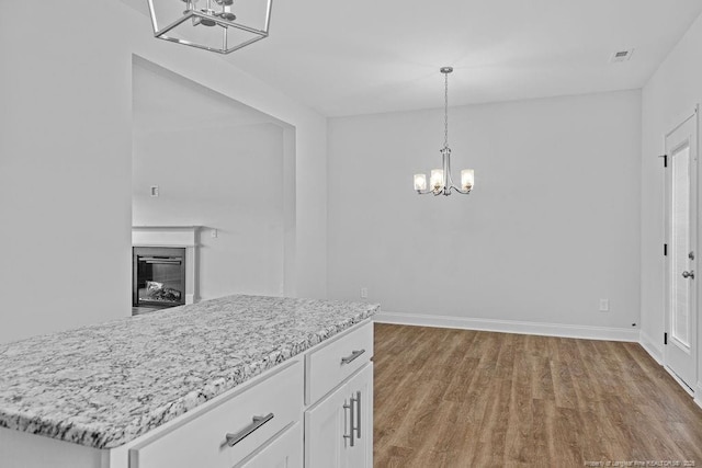 kitchen with visible vents, white cabinets, a glass covered fireplace, wood finished floors, and a notable chandelier