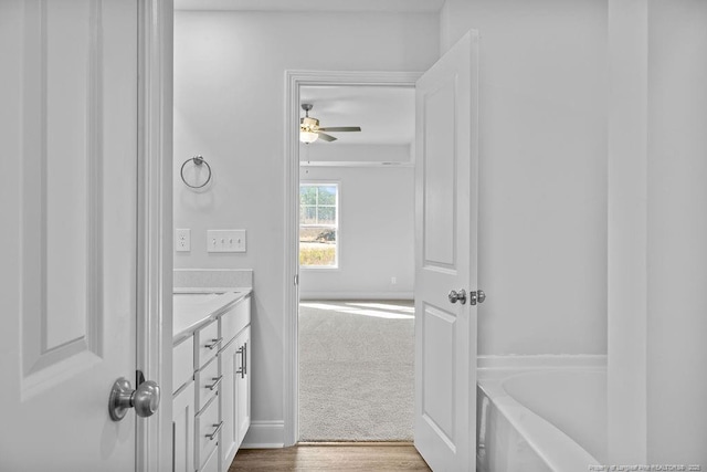 bathroom with a washtub, wood finished floors, vanity, and baseboards