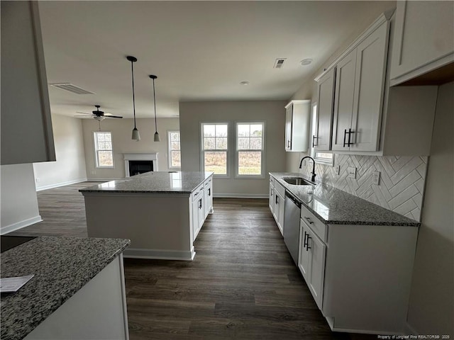 kitchen with a sink, stainless steel dishwasher, dark stone counters, and a kitchen island