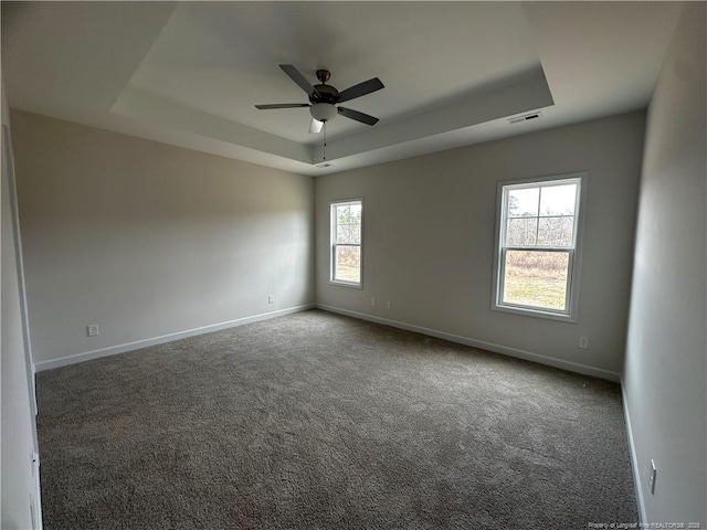 carpeted spare room with a ceiling fan, a tray ceiling, visible vents, and baseboards