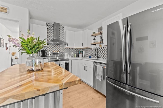 kitchen with sink, stainless steel appliances, wall chimney range hood, tasteful backsplash, and white cabinets