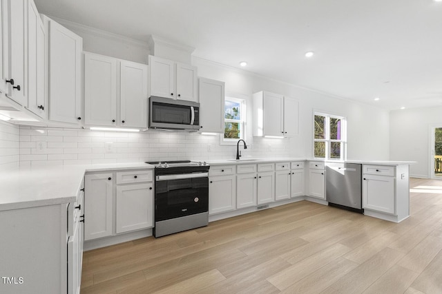 kitchen with light hardwood / wood-style flooring, backsplash, crown molding, white cabinets, and appliances with stainless steel finishes