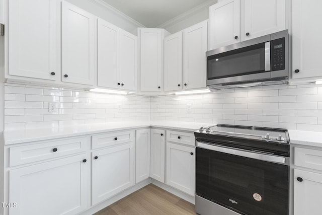 kitchen with light wood-type flooring, backsplash, ornamental molding, stainless steel appliances, and white cabinets