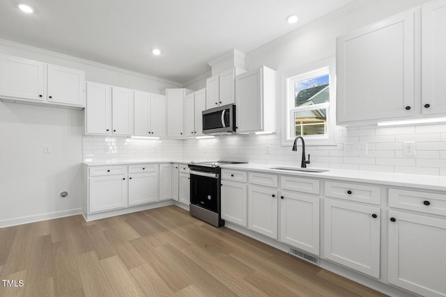 kitchen with white cabinets, sink, ornamental molding, appliances with stainless steel finishes, and light hardwood / wood-style floors