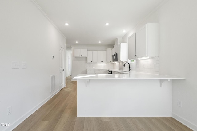 kitchen featuring white cabinets, a kitchen bar, light hardwood / wood-style floors, and kitchen peninsula