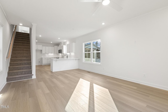 unfurnished living room with crown molding, sink, ceiling fan, and light hardwood / wood-style floors