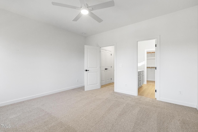 unfurnished bedroom featuring a walk in closet, ceiling fan, a closet, and light carpet