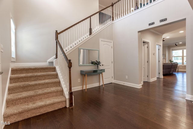 stairs with hardwood / wood-style floors, a towering ceiling, and crown molding