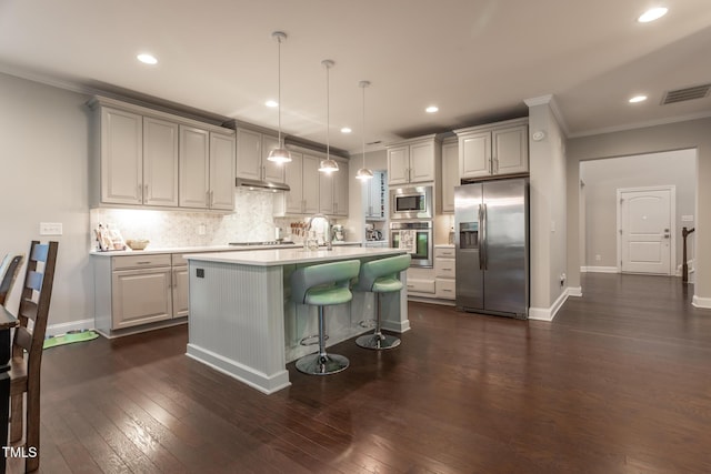 kitchen featuring appliances with stainless steel finishes, dark hardwood / wood-style flooring, a kitchen breakfast bar, a kitchen island with sink, and hanging light fixtures