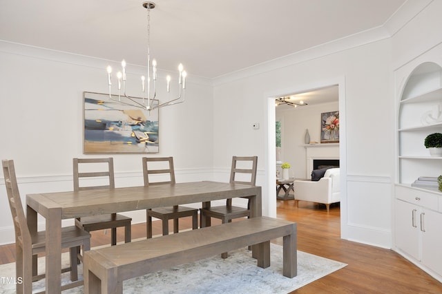 dining room with a chandelier, built in shelves, light hardwood / wood-style flooring, and crown molding